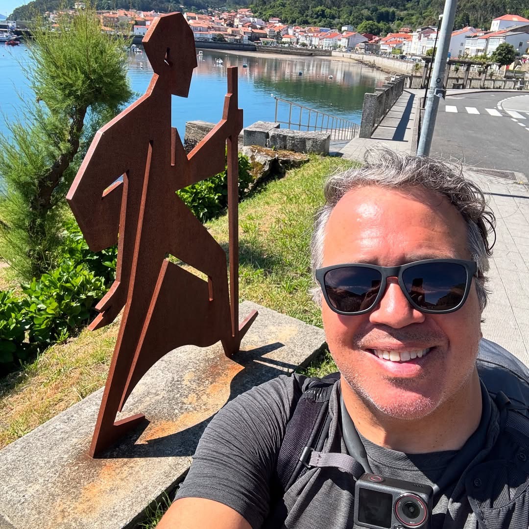 Melvin Rivera smiling warmly while standing on a Camino de Santiago trail, surrounded by rolling hills and vibrant greenery, conveying a sense of happiness and peaceful adventure